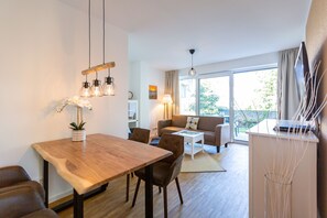 Uma sala de estar moderna com uma mesa de jantar de madeira, cadeiras de couro, um sofá e uma mesa de centro de vidro. Há uma janela grande com cortinas, uma luminária e uma planta sobre a mesa.