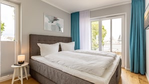 A bedroom with a large bed, a bedside table with a lamp, and a window with curtains.