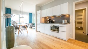 A modern kitchen with white cabinets, a built-in oven, and a dining area with a table and chairs.