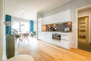 Une cuisine moderne avec des meubles blancs, un four encastré et un coin repas comprenant une table et des chaises.
