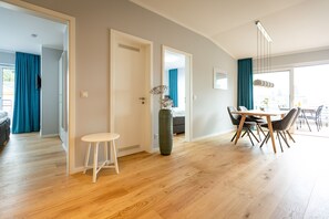 Ein modernes Wohnzimmer mit Essbereich, Holzboden und einem großen Fenster mit Vorhängen.