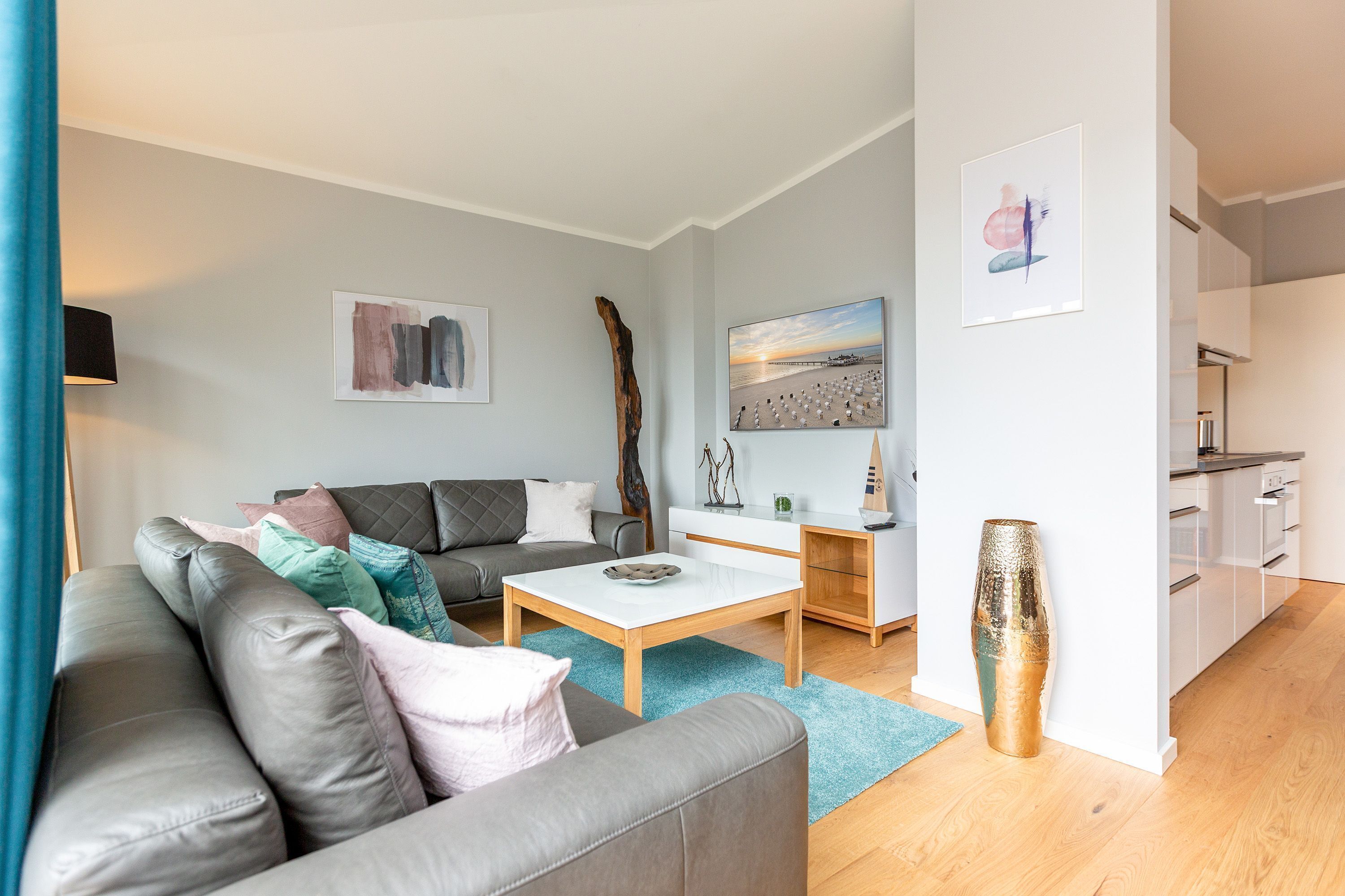 Ein modernes Wohnzimmer mit grauem Sofa, einem Couchtisch und einem Essbereich mit weißem Schrank und einem Gemälde einer Strandansicht.