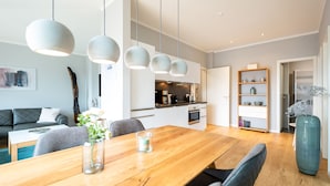 A modern kitchen with white cabinets, a dining area with a wooden table, and pendant lights.