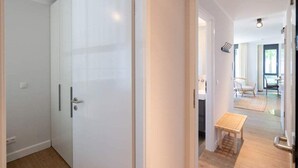 A hallway with a white door, a small wooden bench, and a glimpse of a dining area with chairs and a table. - Villa Maxim, App. 2, Germany (Heringsdorf)