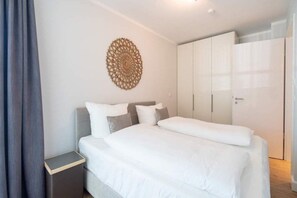 Quarto com cama, mesa de cabeceira, guarda-roupa e um objeto decorativo na parede.