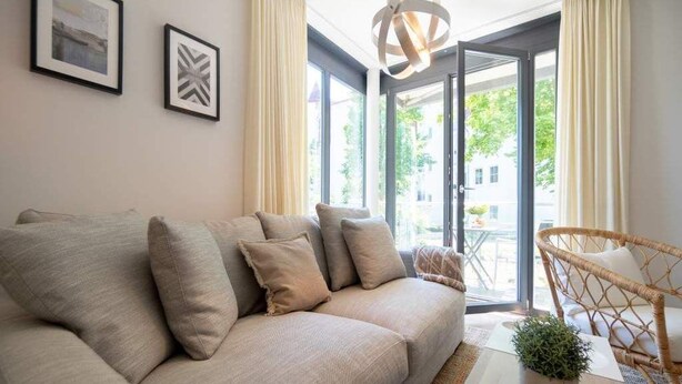 A modern living room with a sofa, a wicker chair, a potted plant, and a large window with a view of greenery outside. - Villa Maxim, App. 2, Germany (Heringsdorf)