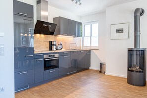 Una cocina moderna con armarios oscuros, estufa de leña y un amplio ventanal.