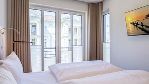 Ein Hotelzimmer mit zwei Betten, großen Fenstern und Blick auf Gebäude.