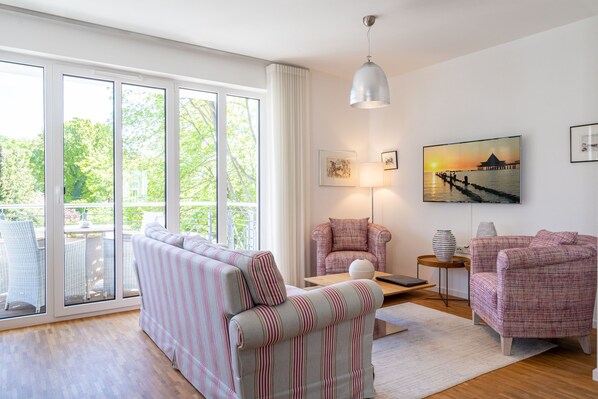A modern living room with a striped sofa, two armchairs, a coffee table, and a painting of a sunset over water.