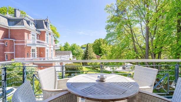 Ein Balkon mit Korbmöbeln und Blick auf ein rot backsteins Gebäude.