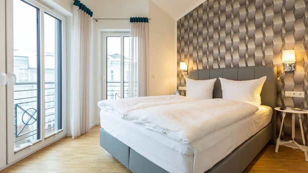 Ein modernes Schlafzimmer mit einem großen Bett, einem Balkon mit Vorhängen und einer Wand mit Muster.