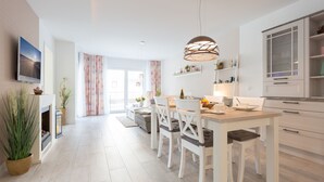 Une cuisine moderne avec des meubles blancs, un coin repas avec des chaises blanches et une grande fenêtre avec des rideaux.
