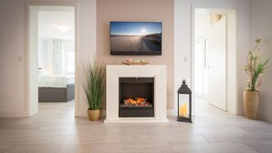 Un salon moderne avec une cheminée, un téléviseur fixé au-dessus et une vue sur la plage par la fenêtre.