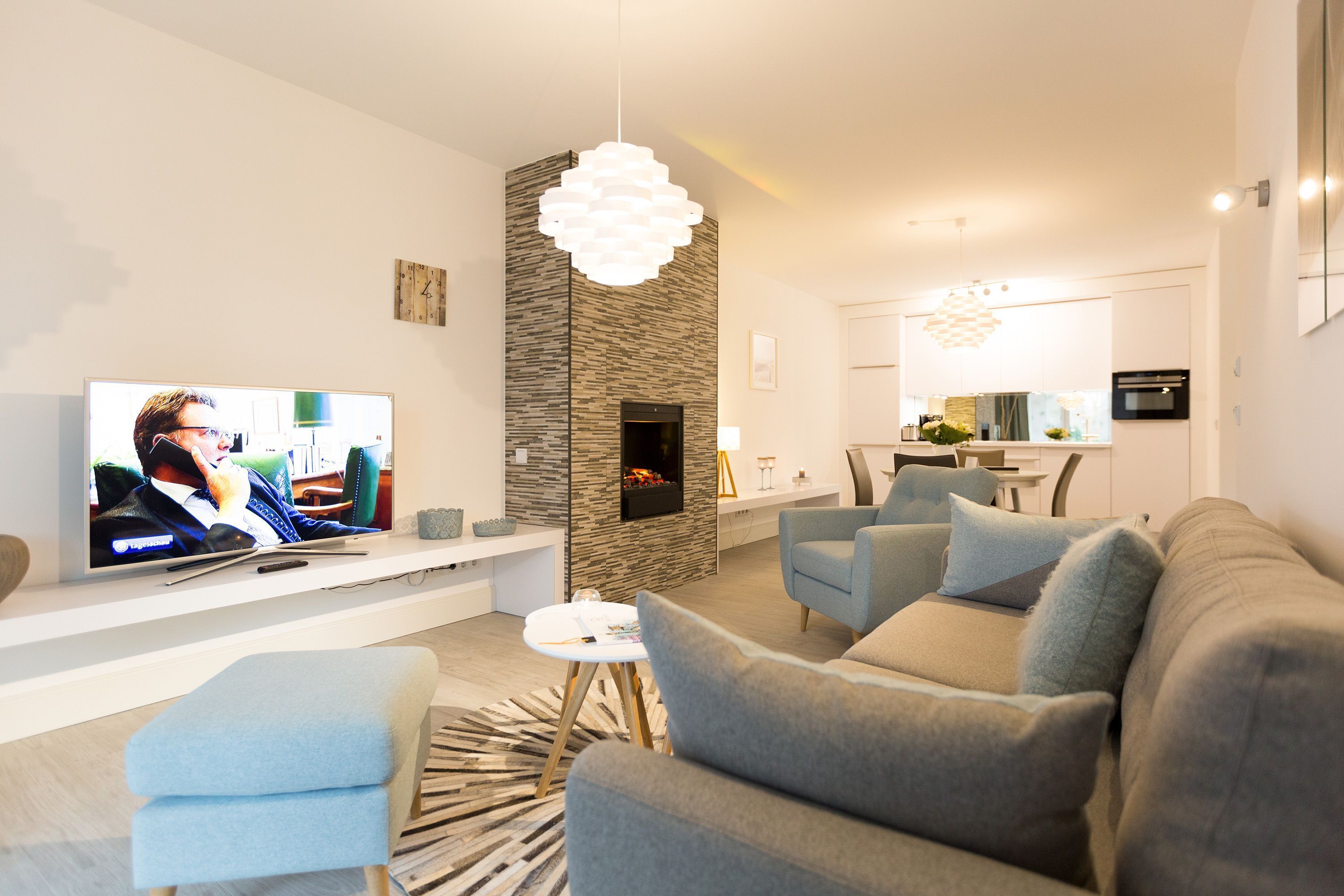 Een moderne woonkamer met een televisie, zithoek en een keuken op de achtergrond.