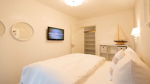 Quarto com cama, televisão, guarda-roupa e pequena mesa com abajur.