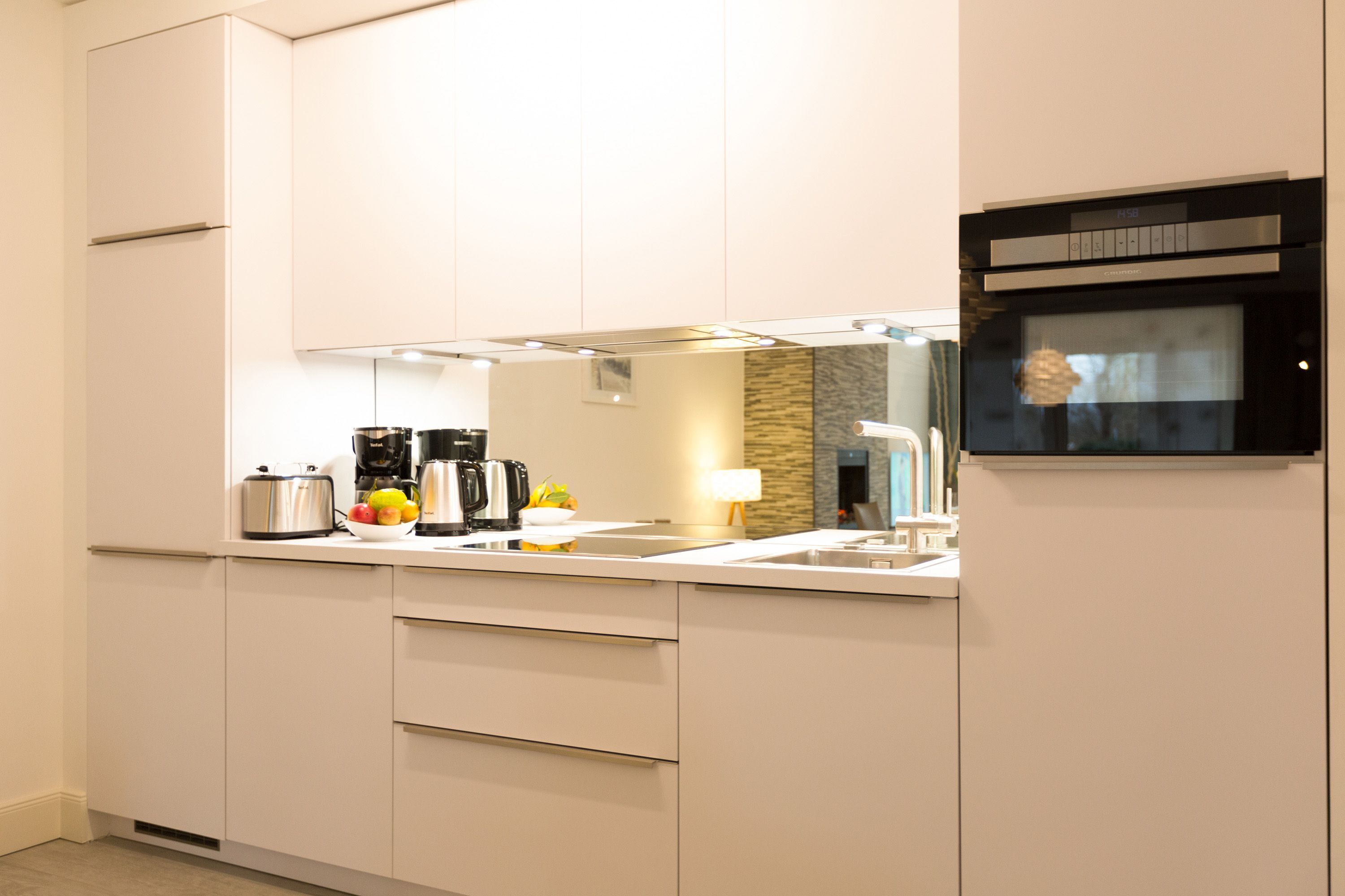 A modern kitchen with white cabinets, a built-in oven, and a countertop with a coffee maker and fruit bowl.