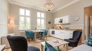 Et moderne køkken med hvide skabe, et spiseområde med blå stole og en lysekrone.