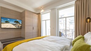 Quarto de hotel moderno com uma cama grande, uma TV na parede e uma janela com vista para edifícios.