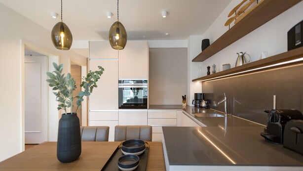 A modern kitchen with a central island, pendant lighting, and a dining area with a table and chairs.