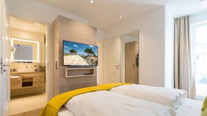 Een moderne hotelkamer met een groot bed, een aan de muur bevestigde televisie, een badkamer met een wastafel en uitzicht op de omgeving.