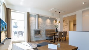 Een moderne woonkamer met een open haard, een eethoek en een keuken die door een open deur zichtbaar is.