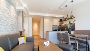 A modern living room with a sofa, coffee table, and dining area. There is a kitchen in the background with a dining table and chairs. - Beachhouse Bansin, app. 04 (Heringsdorf)