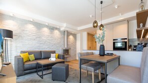 A modern living room with a grey sofa, ottoman, and coffee table, a dining area with a table and chairs, and a kitchen with an oven and microwave. - Beachhouse Bansin, app. 04 (Heringsdorf)