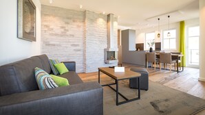 A modern living room with a sofa, coffee table, and a fireplace. There is a dining area with chairs and a table in the background. - Beachhouse Bansin, App. 10 (Heringsdorf)
