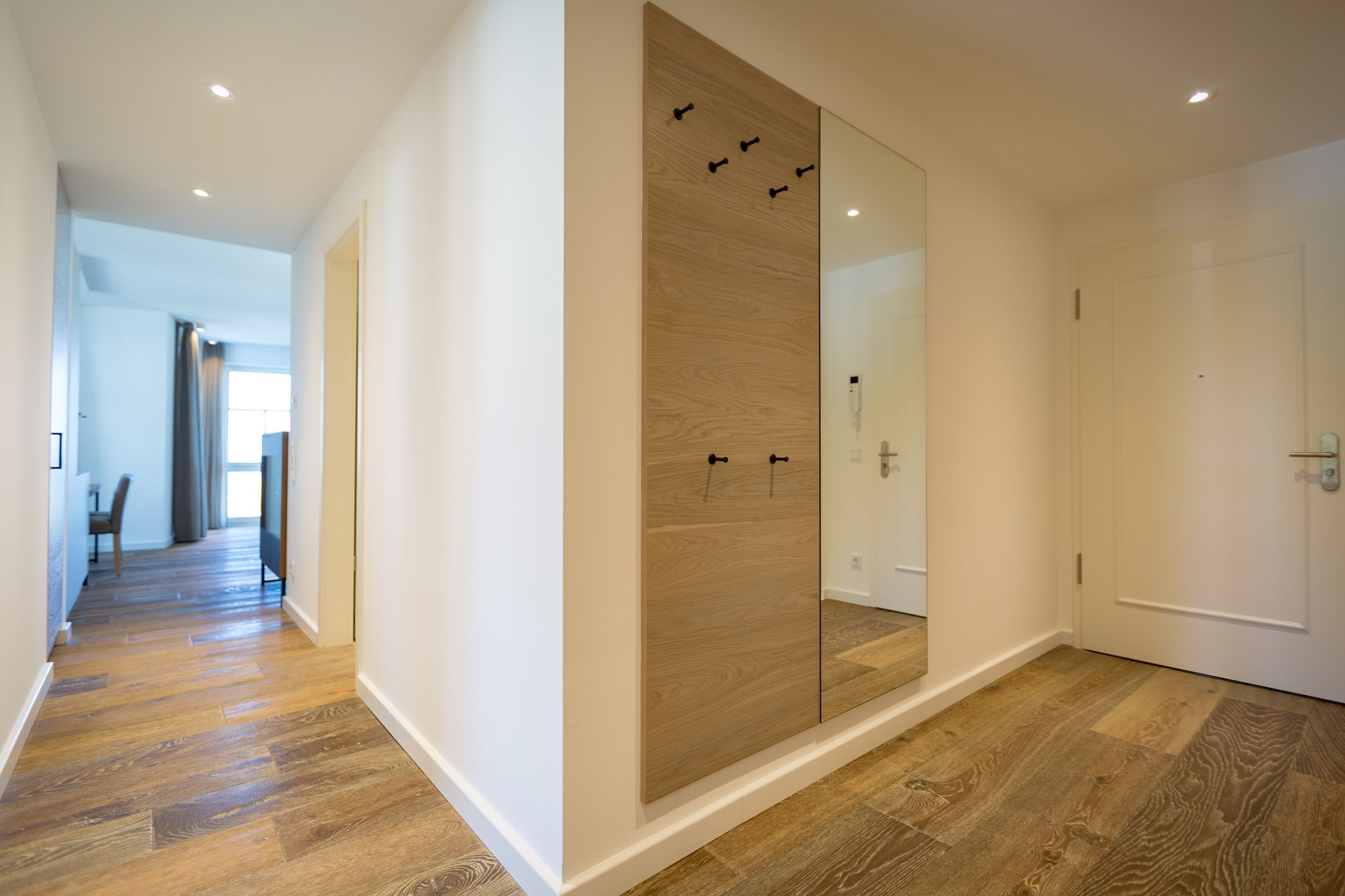 A hallway with wooden flooring, a sliding door with a mirror, and a door with a handle.