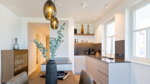 A modern kitchen with a dining area, featuring a wooden table, chairs, a vase with greenery, and a pendant light. - Beachhouse Bansin, App. 01 (Heringsdorf)