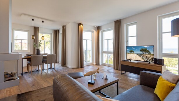 A modern living room with a dining area, large windows, and a flat-screen TV. - Beachhouse Bansin, App. 01 (Heringsdorf)