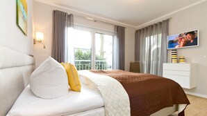 A modern hotel room with a bed, a television, and a view of the outdoors. - Dune Residence Heringsdorf, App. 05 (Heringsdorf)