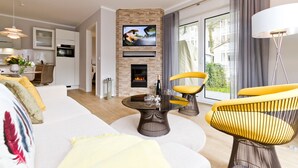 A modern living room with a fireplace, a flat-screen TV, and a dining area with a table and chairs. - Dune Residence Heringsdorf, App. 05 (Heringsdorf)