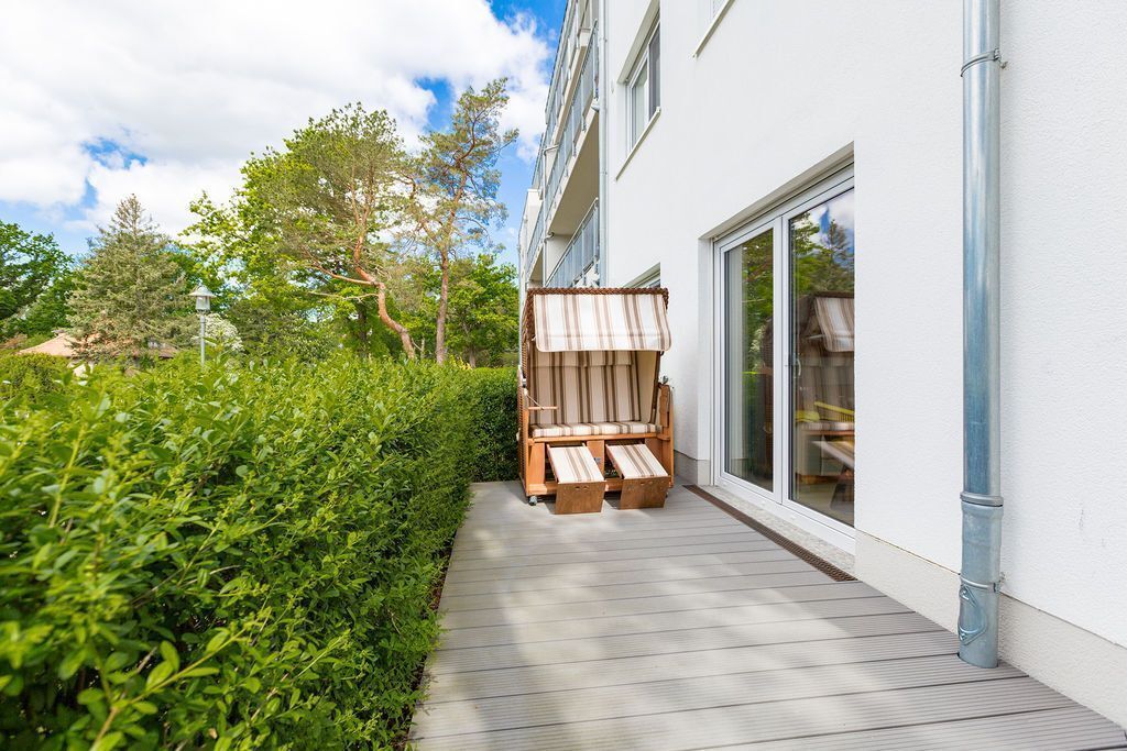 A wooden deck leading to a building with a sliding glass door, surrounded by greenery.