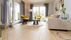 A modern living room with a sofa, two yellow chairs, a round table, and a floor lamp. - Dune Residence Heringsdorf, App. 05 (Heringsdorf)