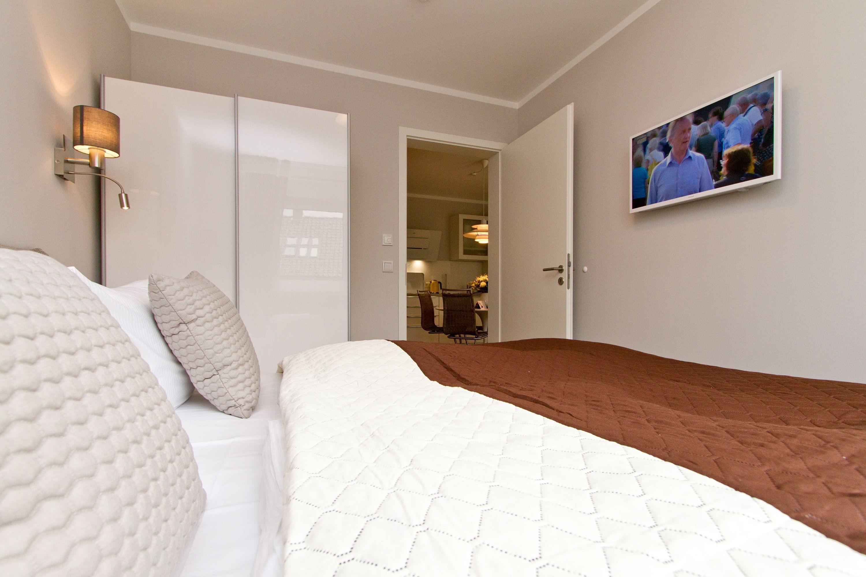 Hotellihuone, jossa on sänky, seinälle asennettu televisio ja vaatekaappi.