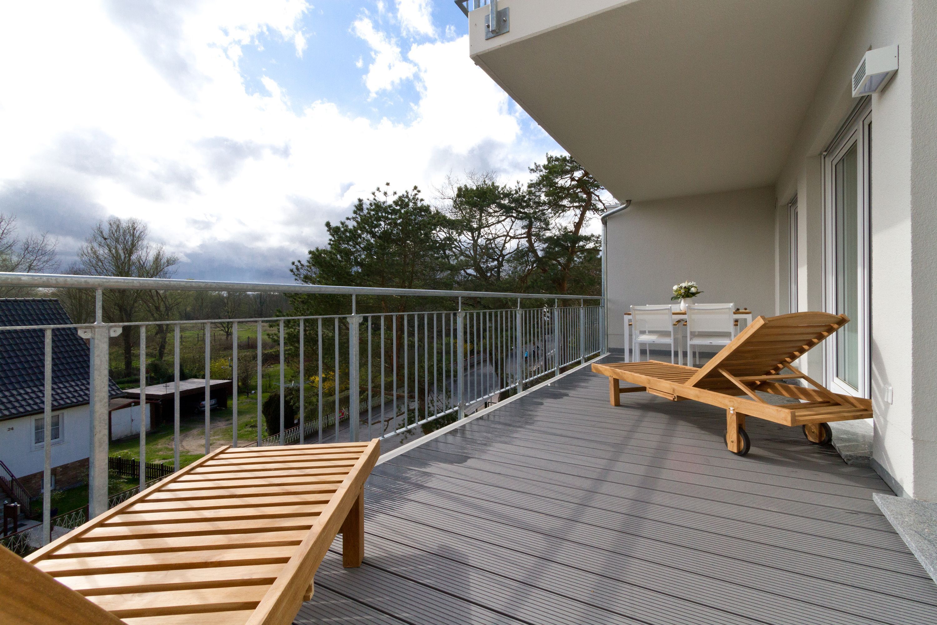 A wooden deck with two lounge chairs and a small table, overlooking a garden and a house.