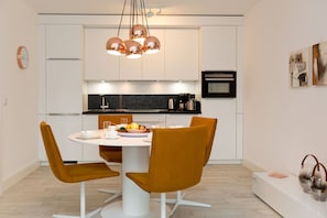 A modern kitchen with white cabinets, a round dining table, and two mustard-colored chairs.