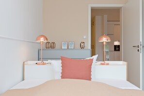 A bedroom with a bed, two bedside tables, a nightstand, a dresser, and two wall-mounted lamps.