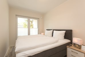 Un dormitorio con cama, mesita de noche, lámpara y ventana con vista a árboles.