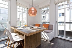 A modern dining area with a wooden table, white chairs, and a copper pendant light. - Villa Westend, apt. 09 (Heringsdorf)