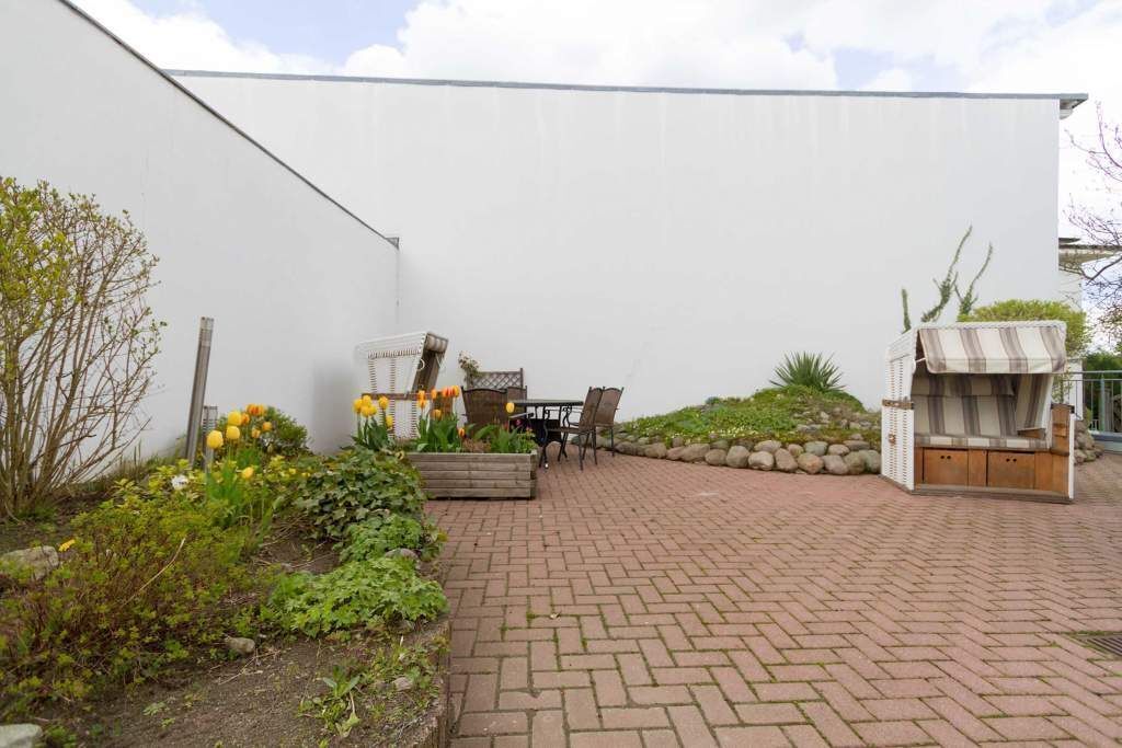 A paved patio with a table and chairs, surrounded by a garden with plants and flowers.