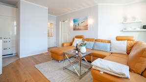 Una sala de estar moderna con una mesa de centro de vidrio, un sofá de cuero naranja y un armario blanco.