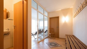 Una habitación con un banco de madera, una mesa pequeña, una lámpara fijada a la pared y un cristalero corredizo que da a un balcón con sillas.
