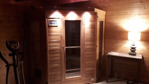 A wooden room with a sauna, a massage table, and a small table with a lamp.
