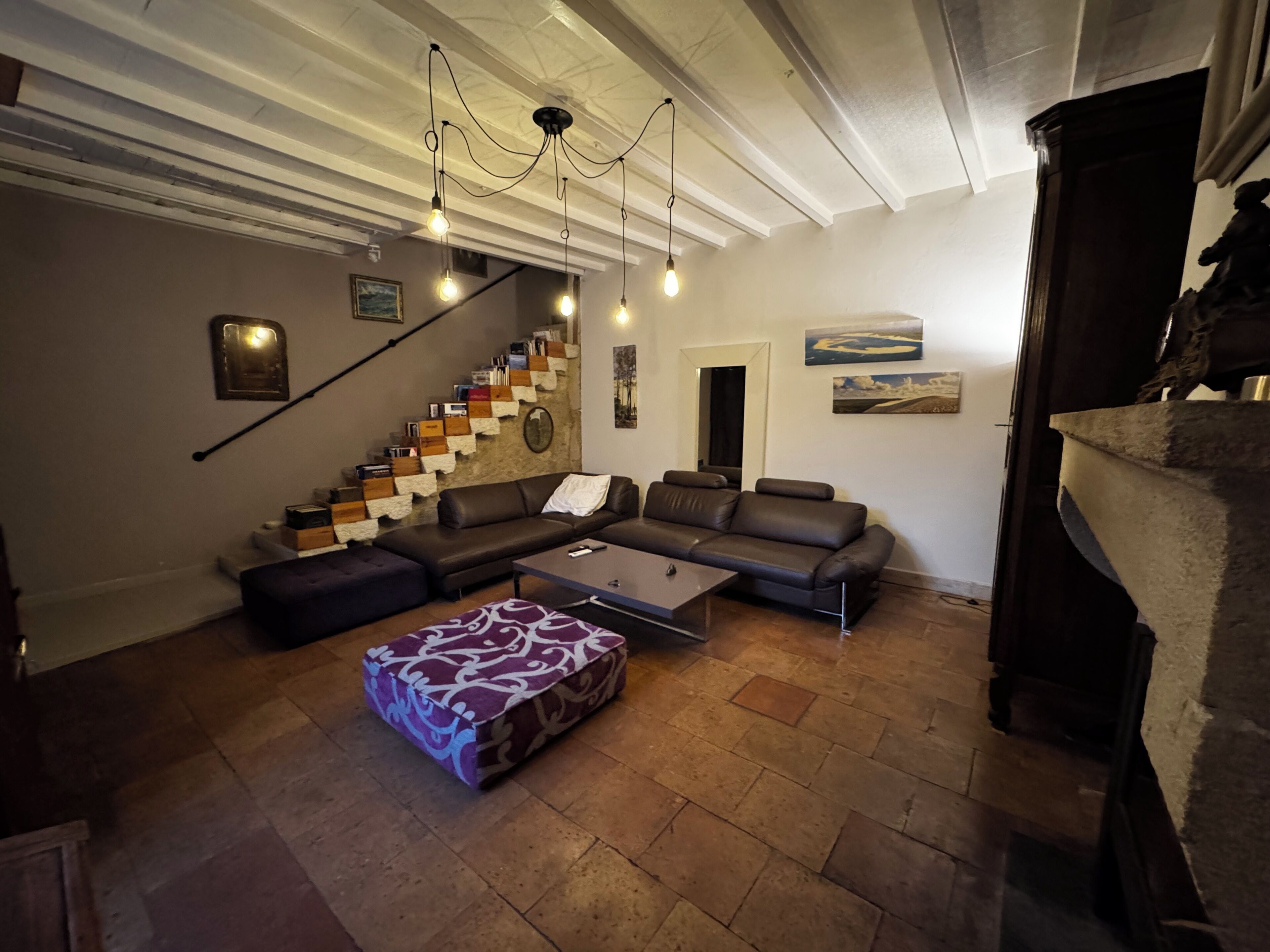 A living room with a staircase, a sofa set, a patterned ottoman, and a fireplace.