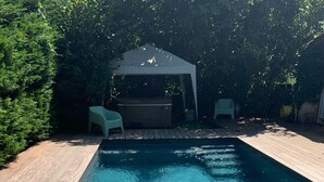 A rectangular swimming pool with clear water, surrounded by a wooden deck and a covered seating area.