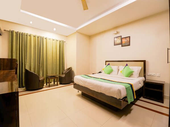 A hotel room with a bed, a chair, a small table, and a nightstand. - Treebo Time Square Marine Drive (Kanayannur)