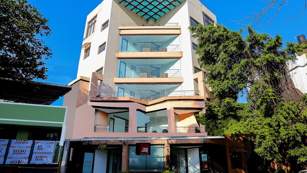 A modern building with a glass facade, multiple floors, and a prominent entrance with a staircase. - Treebo Time Square Marine Drive (Kanayannur)