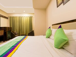 A hotel room with a bed, green curtains, a desk, and a chair. - Treebo Time Square Marine Drive (Kanayannur)